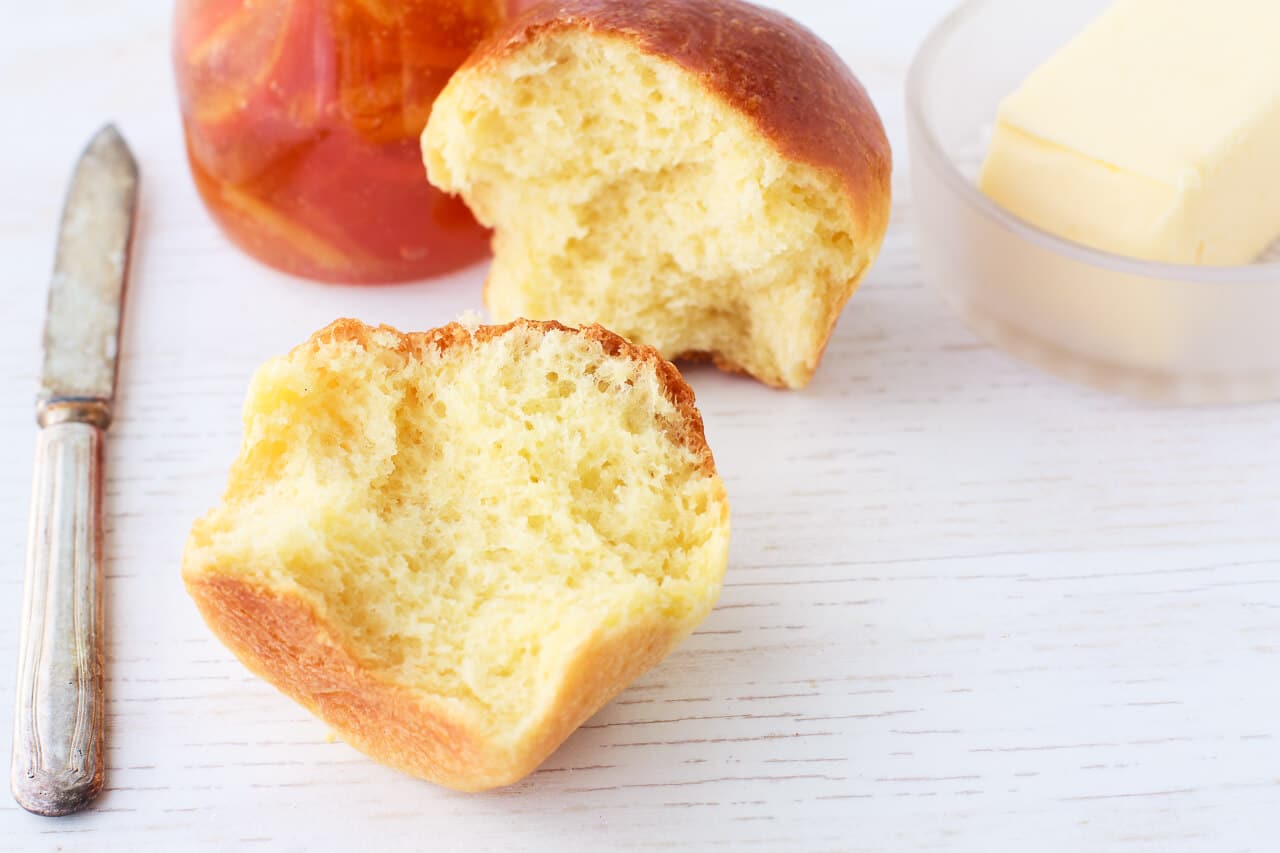 Homemade brioche brun split open to reveal a fluffy golden interior, served with butter and a knife