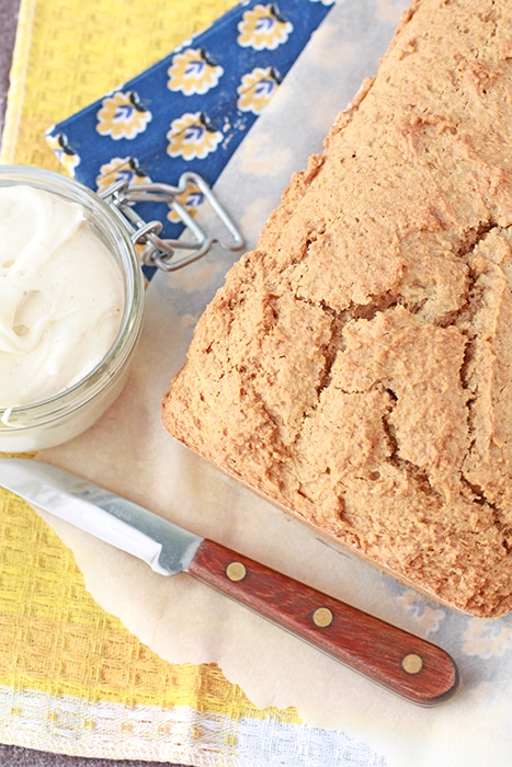 Overhead view of a pumpkin bread with a jar of cream cheese frosting on yellow and blue linens