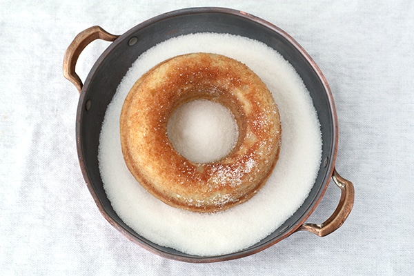 baked donut in a dish of granulated sugar to coat it all around