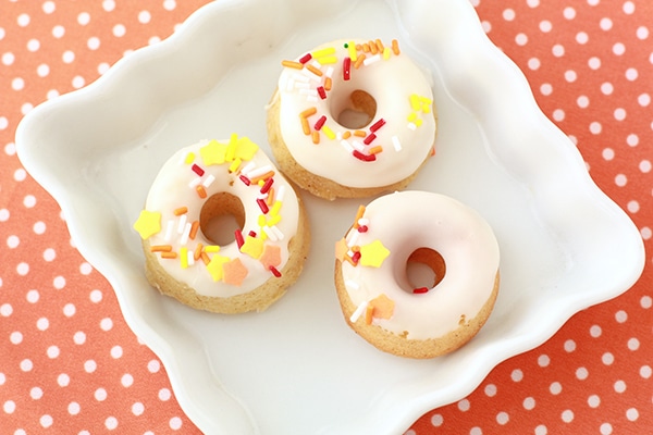 Mini pumpkin donuts with a white icing glaze and yellow, red, and orange sprinkles