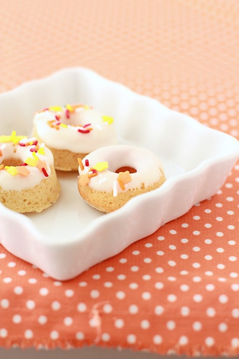 Three mini glazed pumpkin donuts on a white dish on a orange and white polka dot tablecloth 