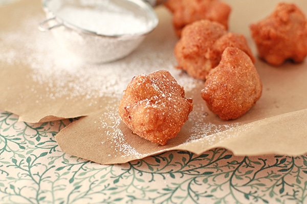 beer apple fritters on brown paper with icing sugar in a small strainer for dusting
