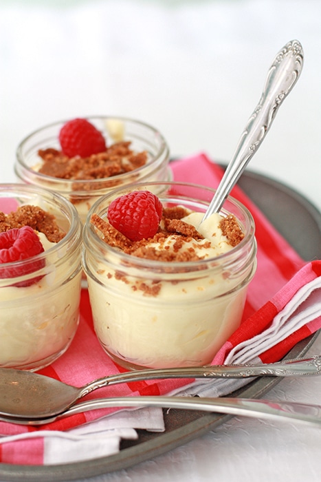 Little jars of lemon mousse served with graham cracker crumble and fresh raspberries with pink striped napkin