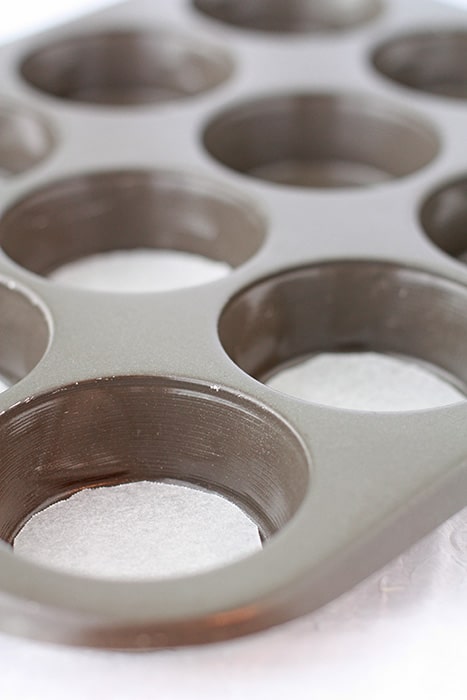 Preparing a muffin pan for baking by lining the bottom of each well with a round of parchment