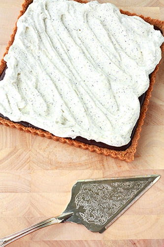 a square chocolate tart on a wood board topped with swirls of Earl grey whipped cream