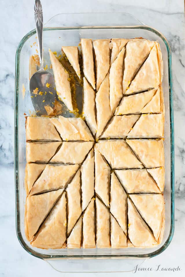 A glass pan of homemade pistachio baklava being served with a small lifter