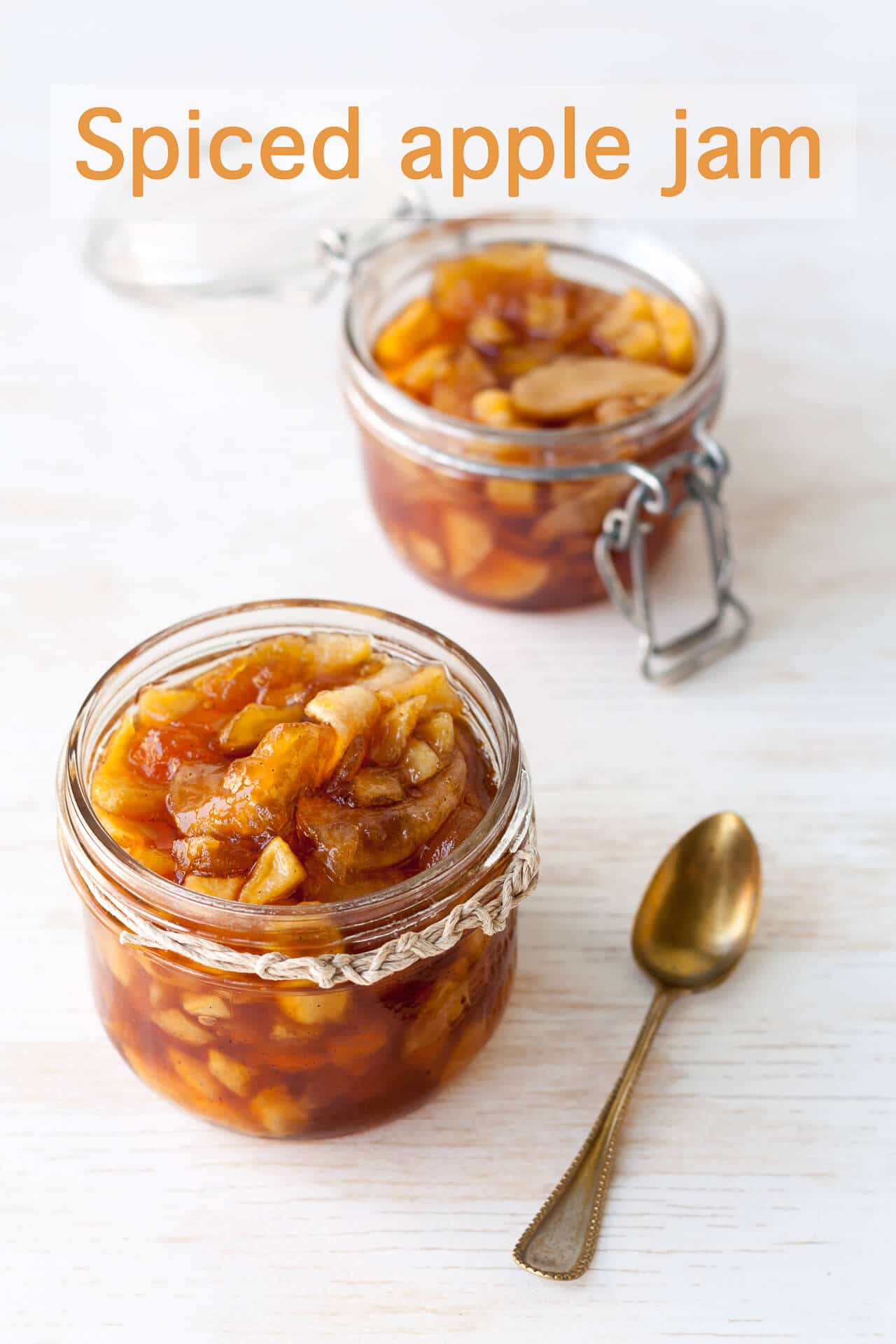 Two jars of spiced apple jam made with chunks of apple and served with a teaspoon