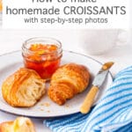 Homemade croissants served on a white enamelware plate with a blue rim and a jar of orange marmalade, blue and white striped napkin, knife with