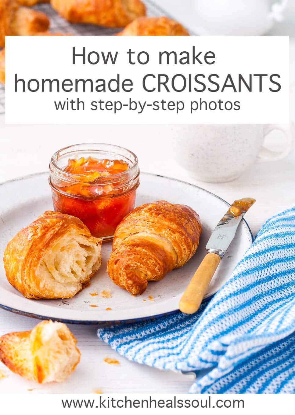 Homemade croissants served on a white enamelware plate with a blue rim and a jar of orange marmalade, blue and white striped napkin, knife with