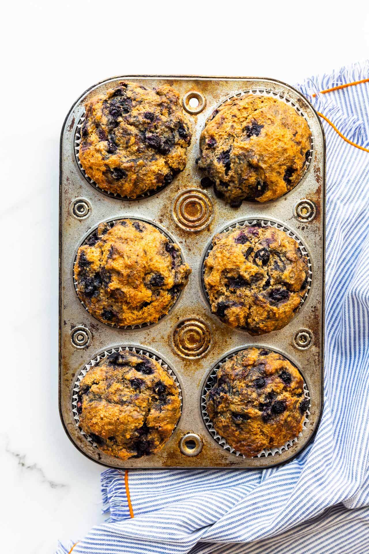 Baked blueberry bran muffins in a vintage muffin pan with a blue and white striped linen with orange edging