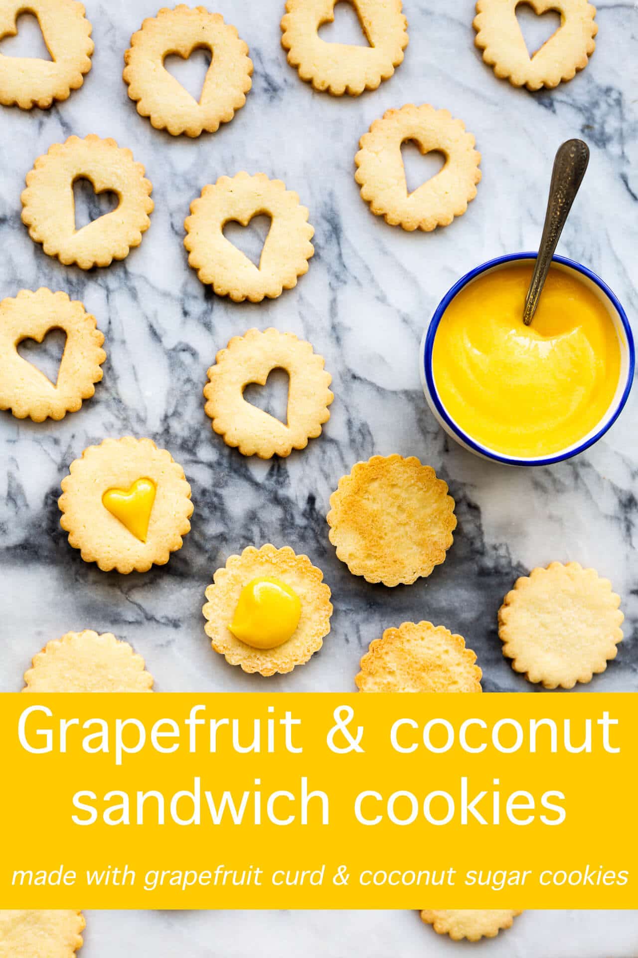 Golden buttery coconut crinkle cut round cookies with heart cut out for sandwiching with bright grapefruit curd in a bowl with a spoon