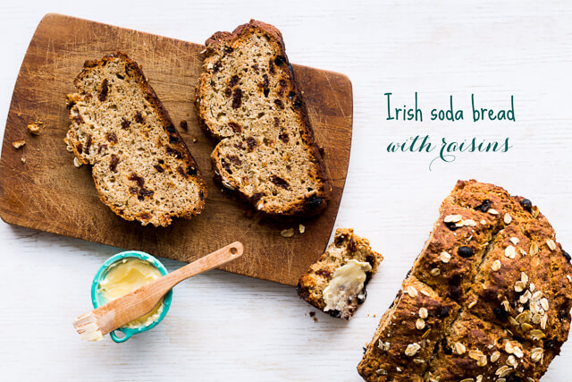 Sliced loaf of Irish soda bread with raisins served with softened butter on a dark wood cutting board