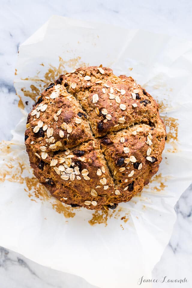 A golden brown loaf of Irish soda bread with raisins topped with oats and scored with an X