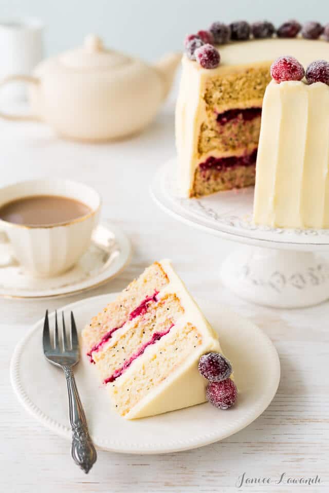 Cranberry cardamom cake sliced with cream cheese frosting and sugared cranberries