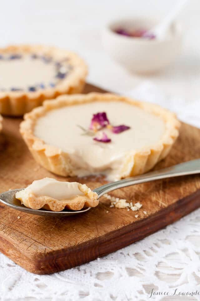 Little Earl Grey panna cotta tarts decorated with dried rose petals and dried cornflower, cut into with a spoon