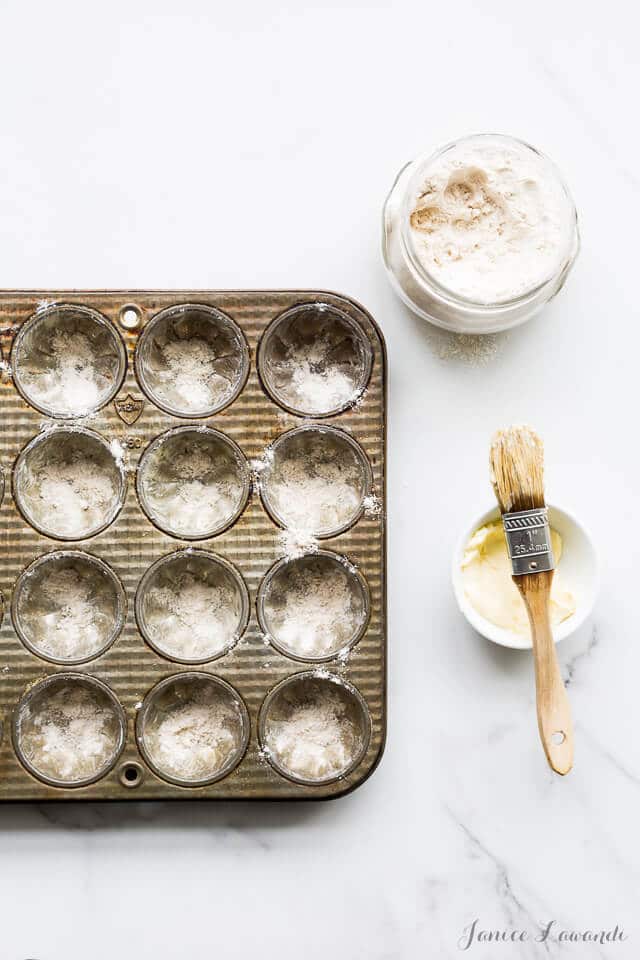 Cake pan prep for financiers by buttering each pan cavity and dusting with flour