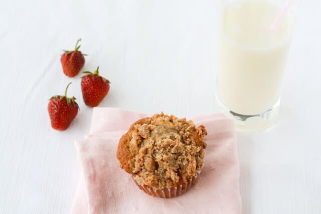 Strawberry rhubarb muffins topped with a crumble topping served with a glass of milk and fresh strawberries