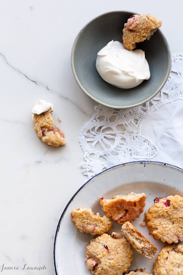 Little rhubarb scones on a plate served with a small bowl of sweetened whipped cream.