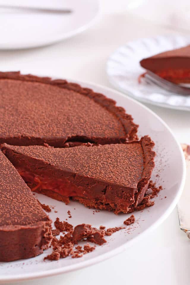 Sliced chocolate tart with piece removed to reveal layer of pink rhubarb compote under the ganache