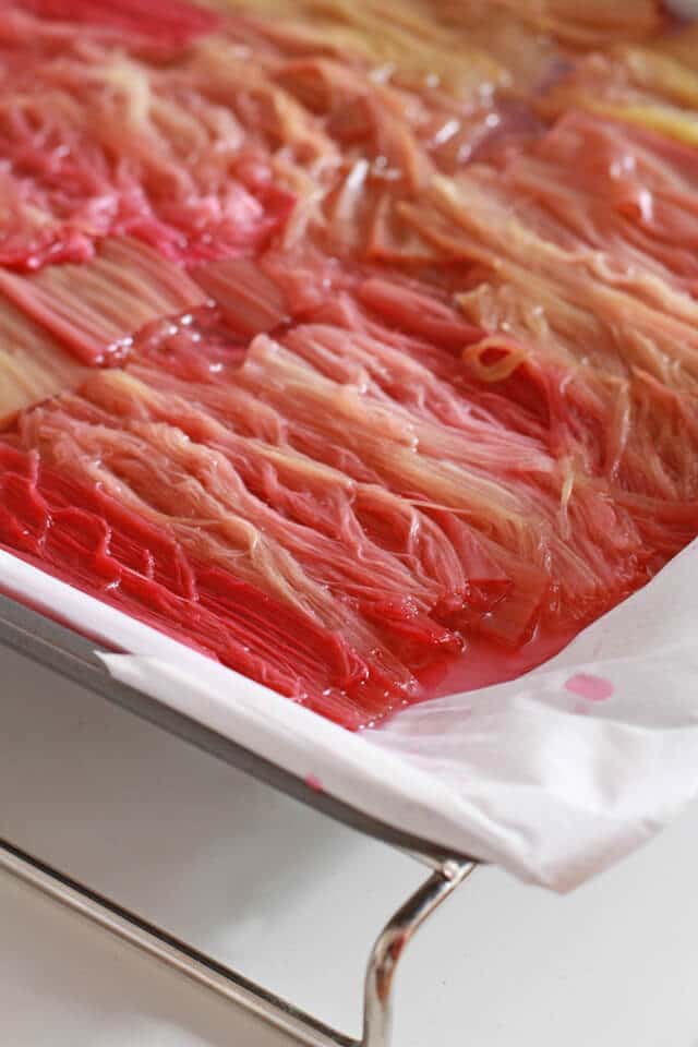 Roasted rhubarb cooling on a parchment-lined sheet pan set on a wire cooling rack.