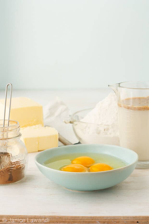 spice cake ingredients featuring butter, eggs, cinnamon, flour in a blow and a measuring cup with milk and vanilla extract