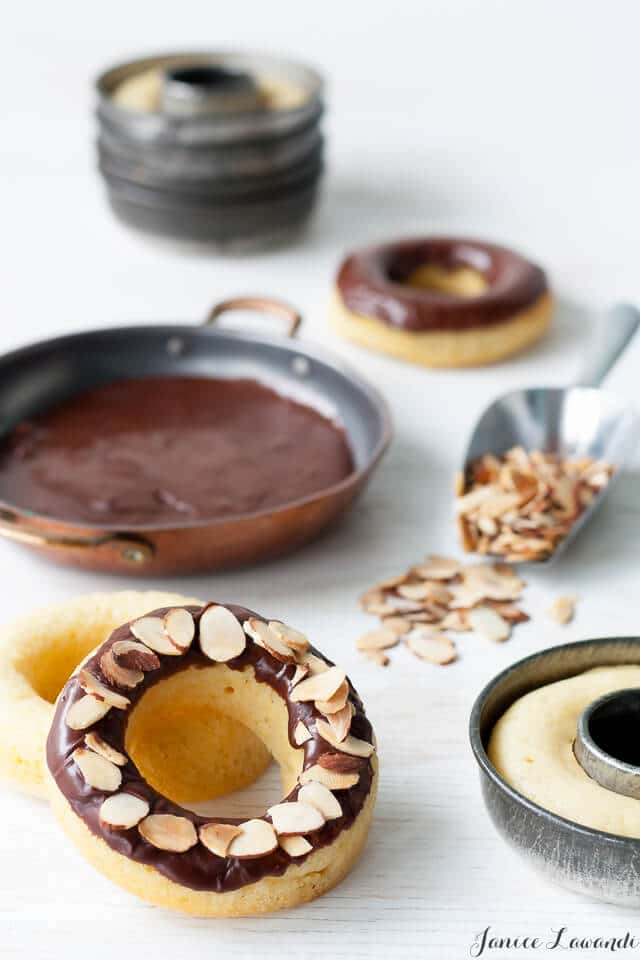 Image of making baked donuts in vintage donut pans, dipped in shallow dish of chocolate glaze and coated with sliced almonds in a scoop