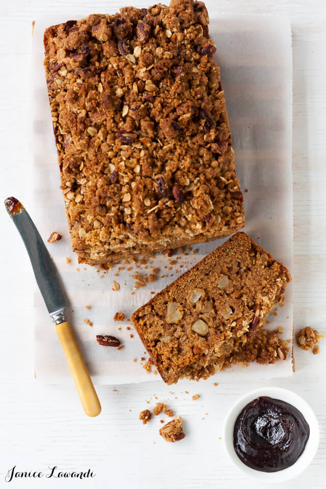 Brandy apple loaf cake sliced on parchment-lined cutting board with a knife and apple butter to serve with it.