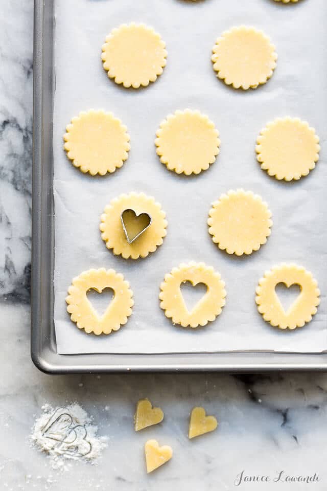 Cutting out coconut cookies with crinkle edged round cookie cutter and then cutting out little heart from centre to make window for linzer cookies