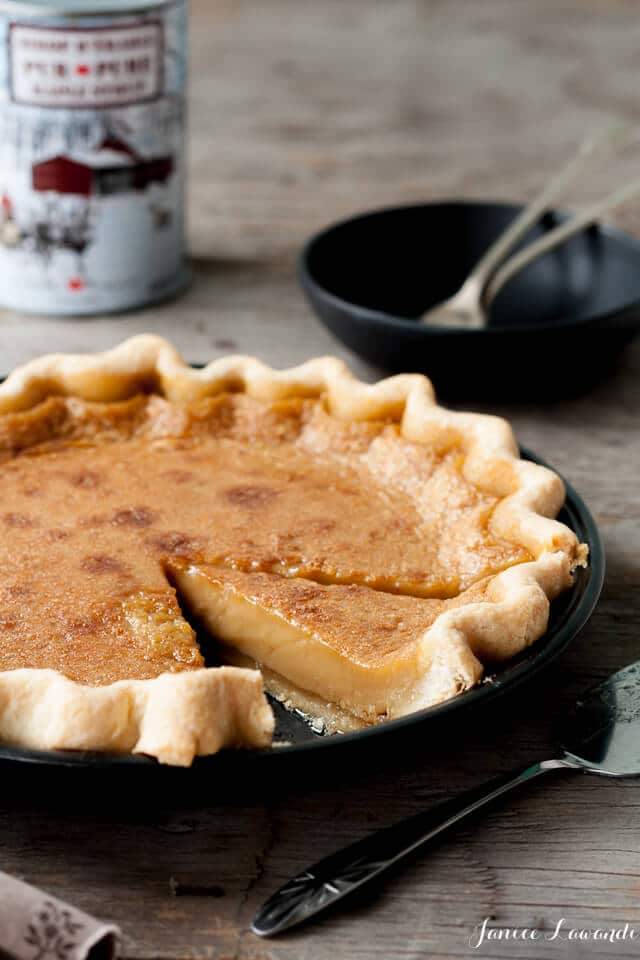 Maple-syrup pie sliced to show the perfect maple custard filling set after baking and chilling, with a traditional maple syrup can from Quebec in the background and black plates