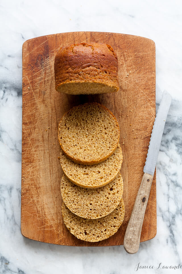 Quebec brown bread sliced on a wood cutting board with serrated knife set on a marble surface