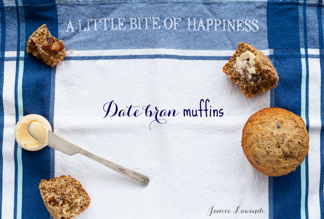 Date bran muffins served with butter and butter knife on a tea towel with blue plaid print and "A little bite of happiness" text printed on towel