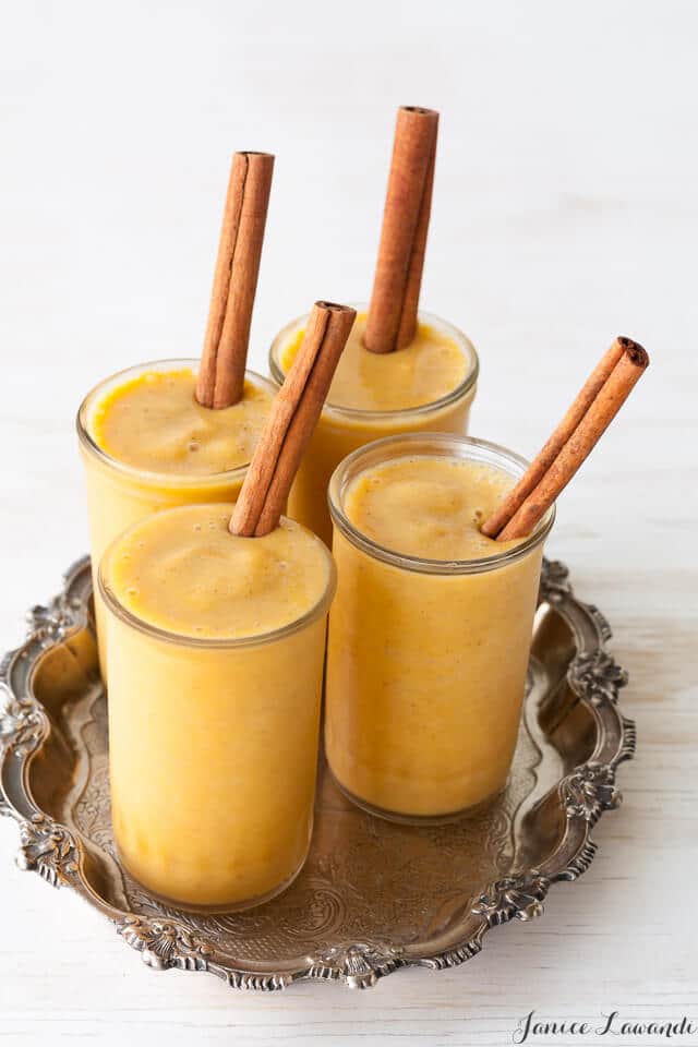 4 glasses of orange pumpkin spice shakes garnished with cinnamon sticks.