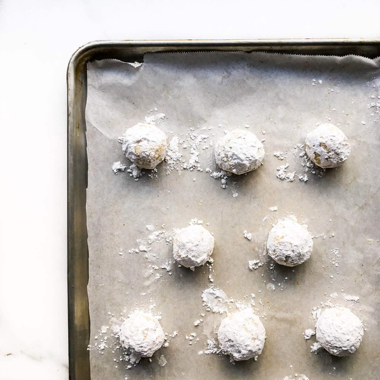 Balls of lemon ricotta cookie dough are rolled in icing sugar before baking on a parchment-lined sheet pan to give them a cracked finish.