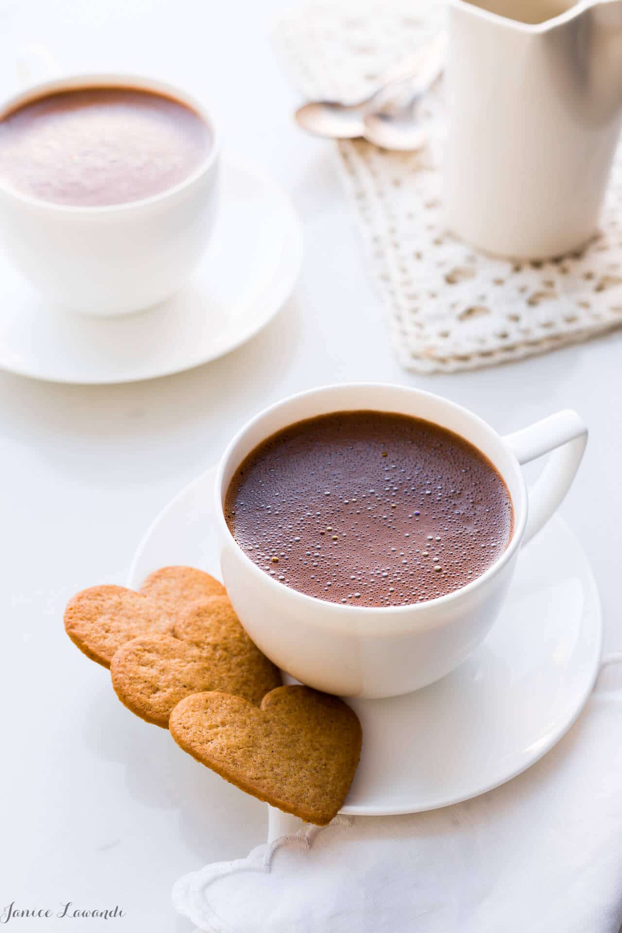 Homemade hot chocolate served in white cups, white saucers, and heart-shaped cookies.