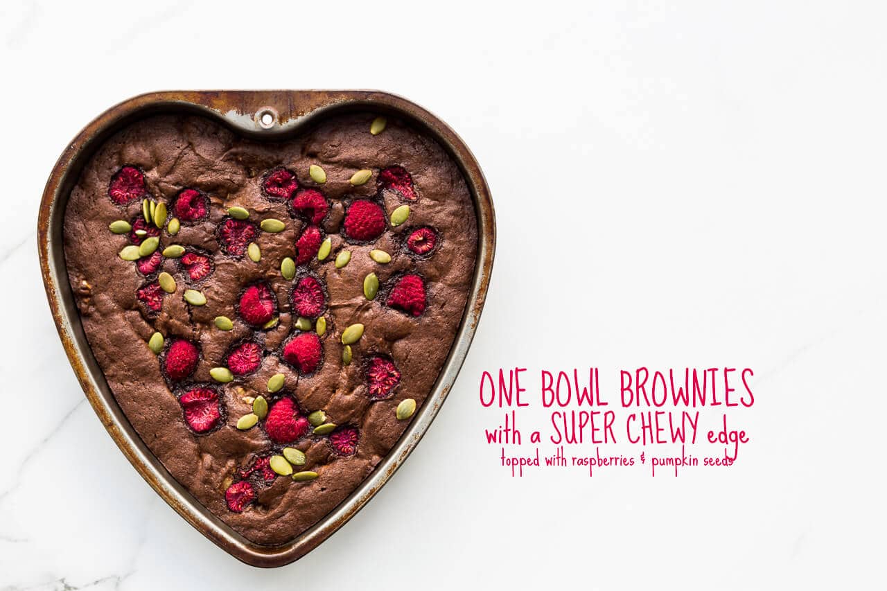 A recipe for one bowl brownies with walnuts and a super chewy edge, baked in a heart shape pan and topped with raspberries and pumpkin seeds