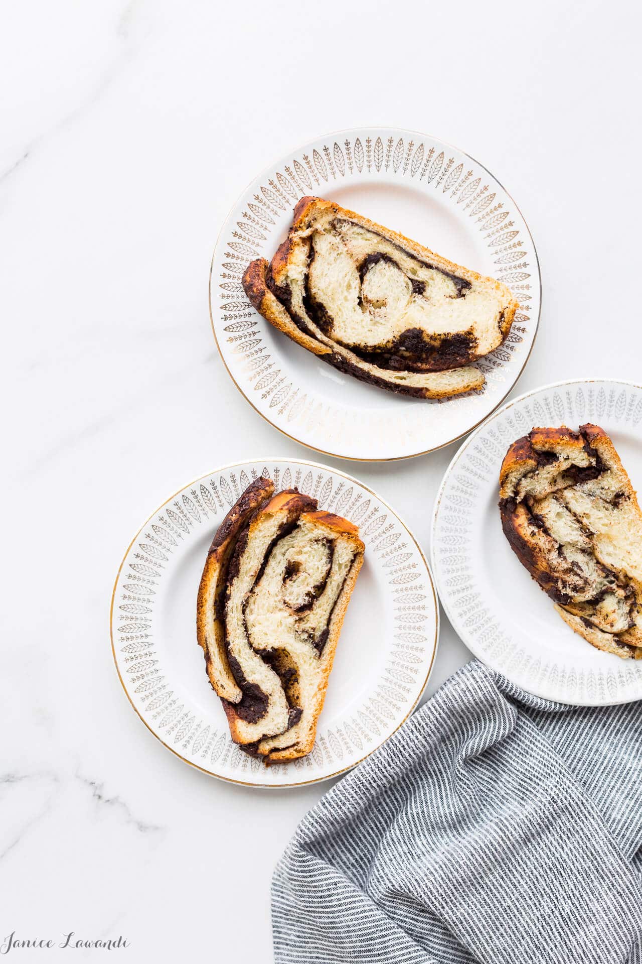 Slices of chocolate babka bread on white plates with a striped napkin