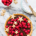 Milk chocolate ganache tart made with a coffee cookie crust and topped with fresh raspberries and cookie stars