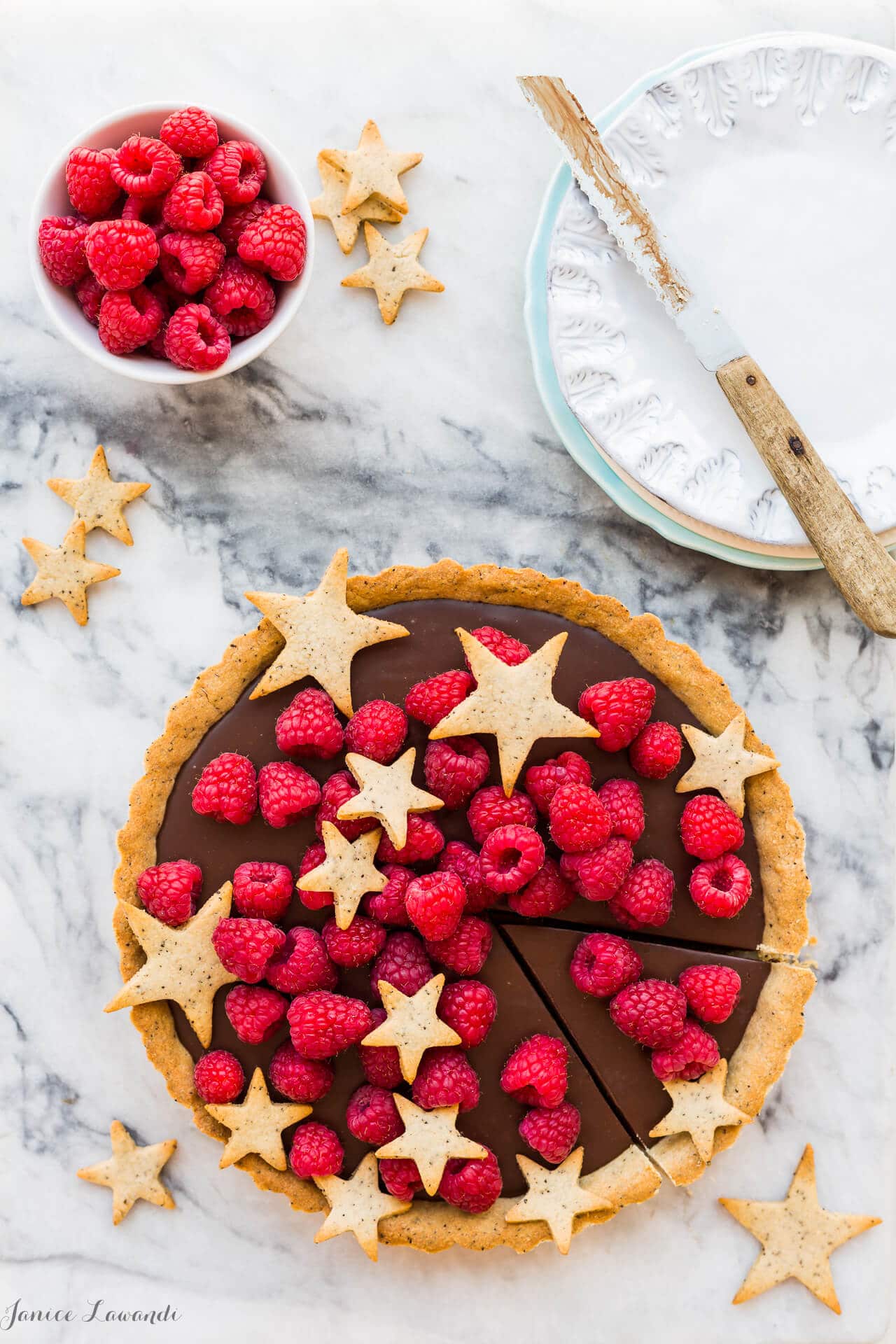 Milk chocolate ganache tart made with a coffee cookie crust and topped with fresh raspberries and cookie stars.