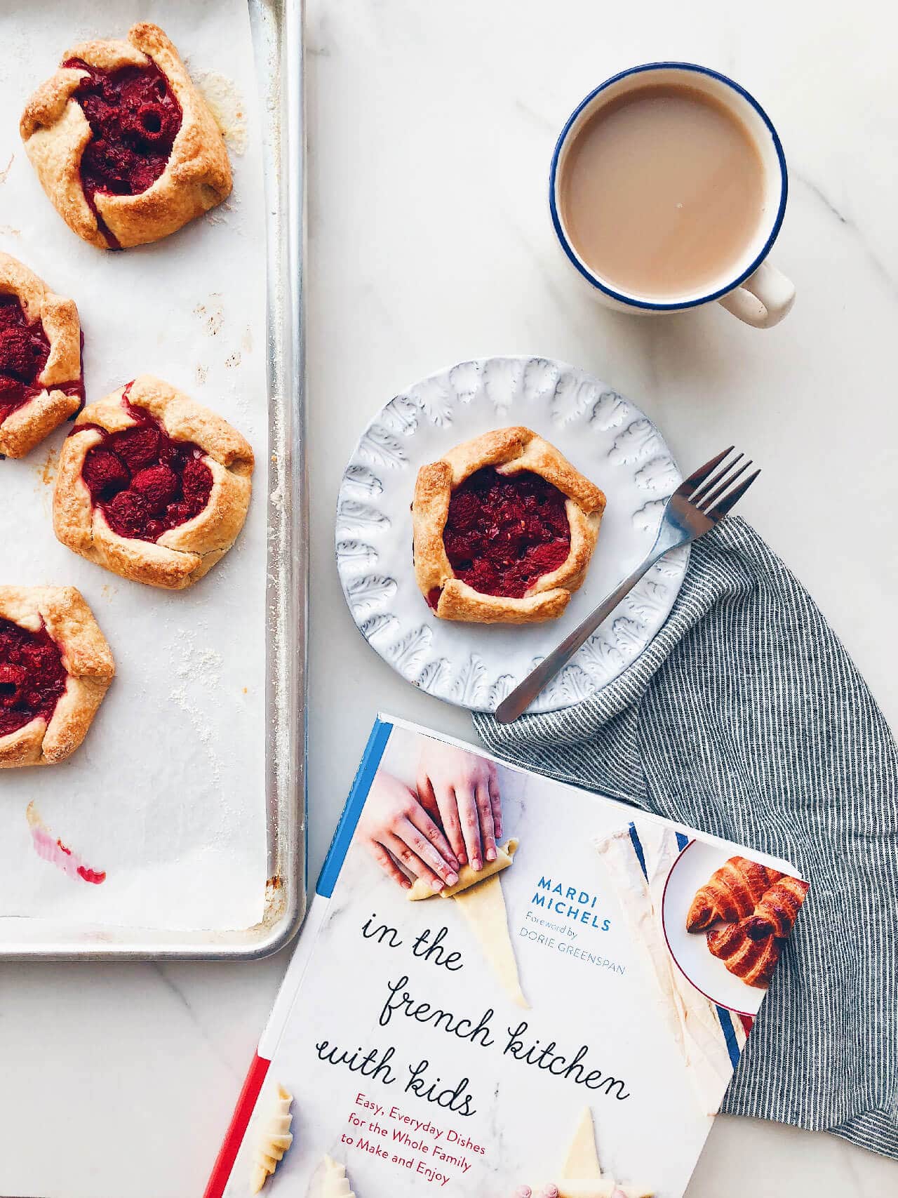 Baked mini raspberry galettes shown next to the book In the French Kitchen With Kids by Mardi Michels