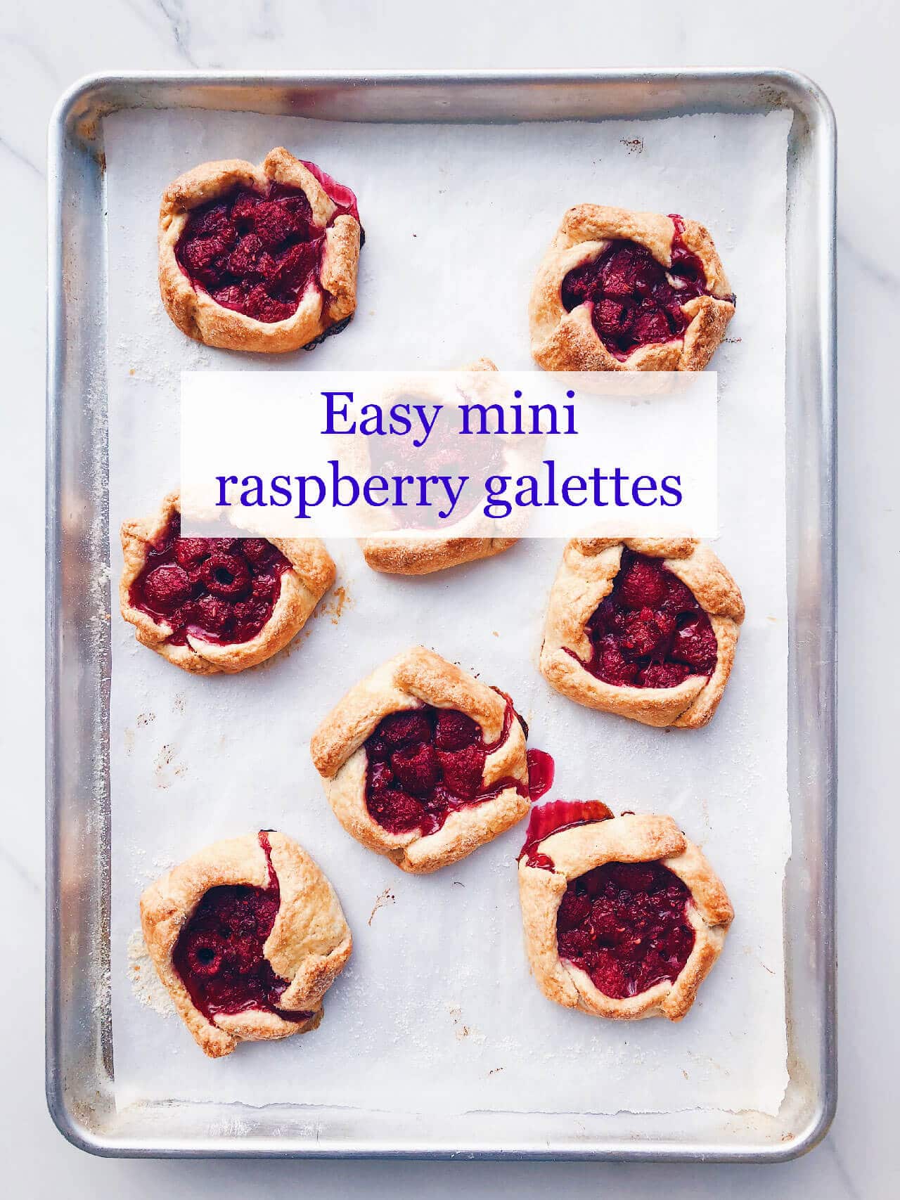 mini raspberry galette pies cooling on a parchment-lined baking sheet 