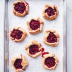 Freshly baked mini raspberry galettes on a parchment-lined baking sheet