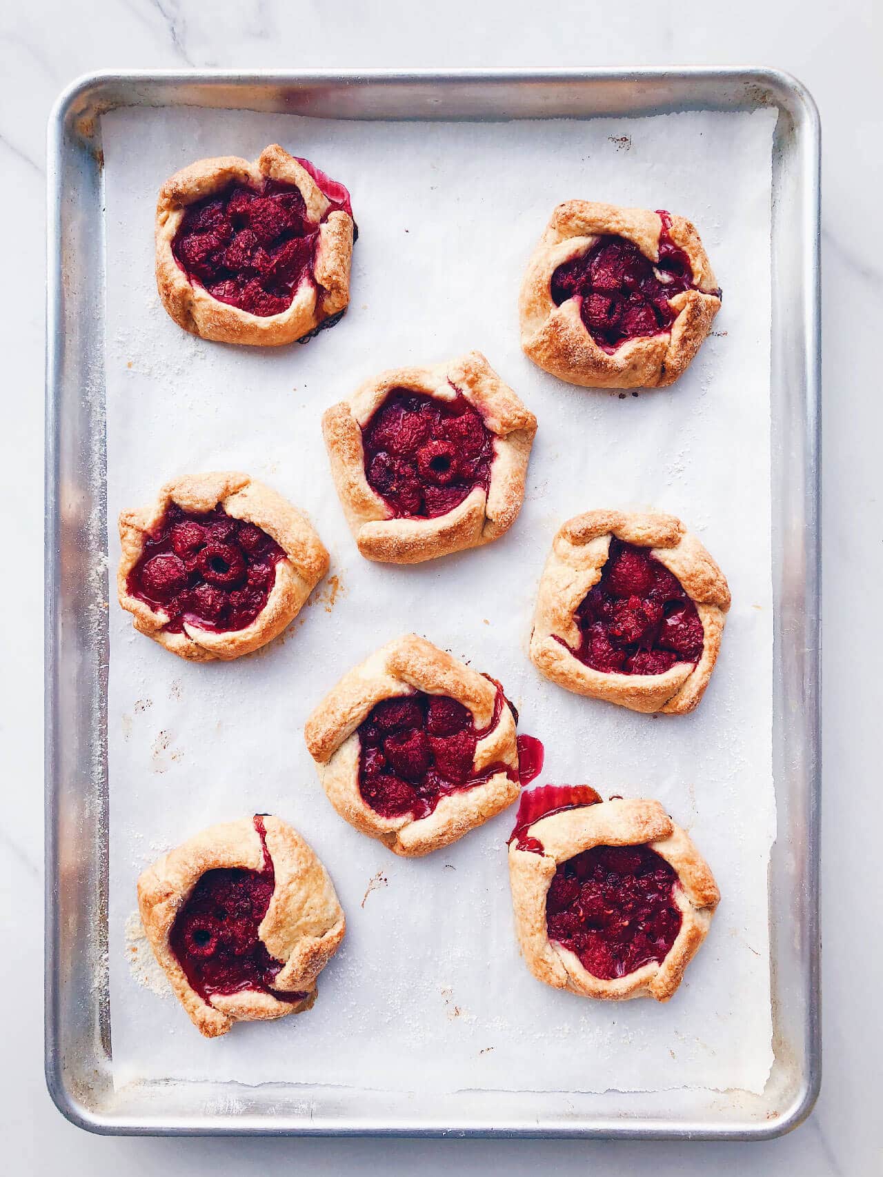 Freshly baked mini raspberry galettes on a parchment-lined baking sheet