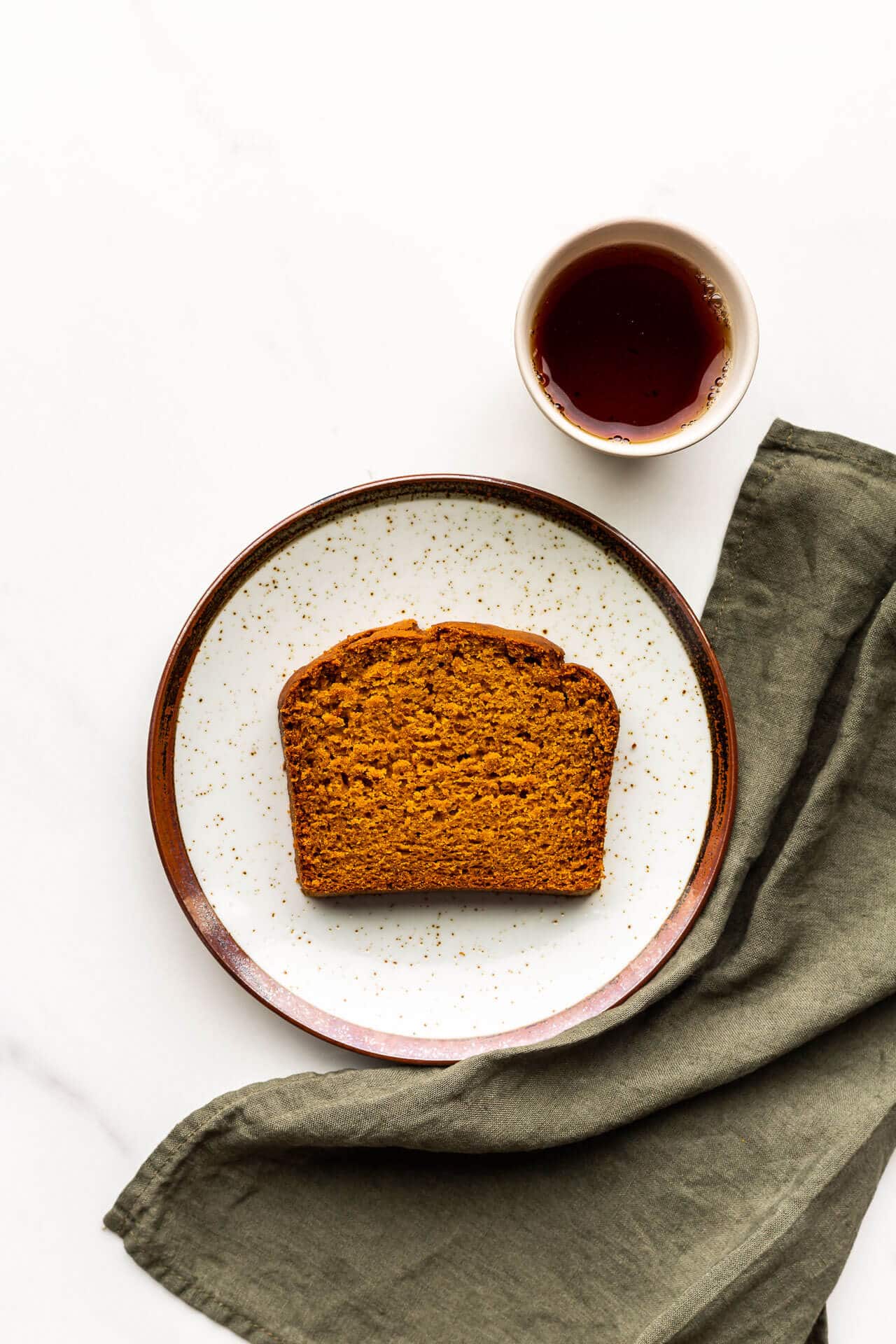 A slice of pumpkin spice loaf cake with a cup of tea and a green linen.