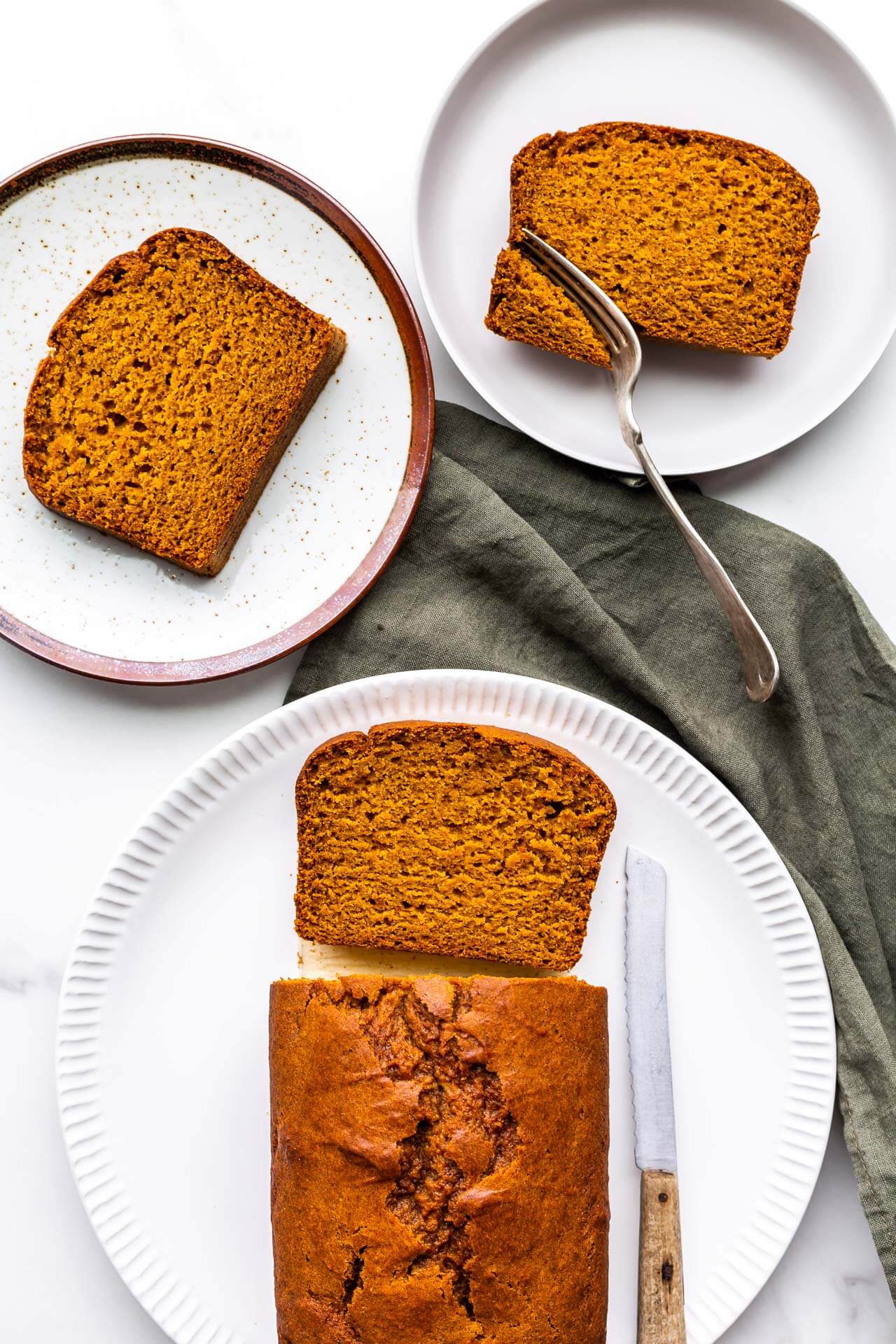 Slicing pumpkin loaf cake to serve on ceramic plates with green linen.