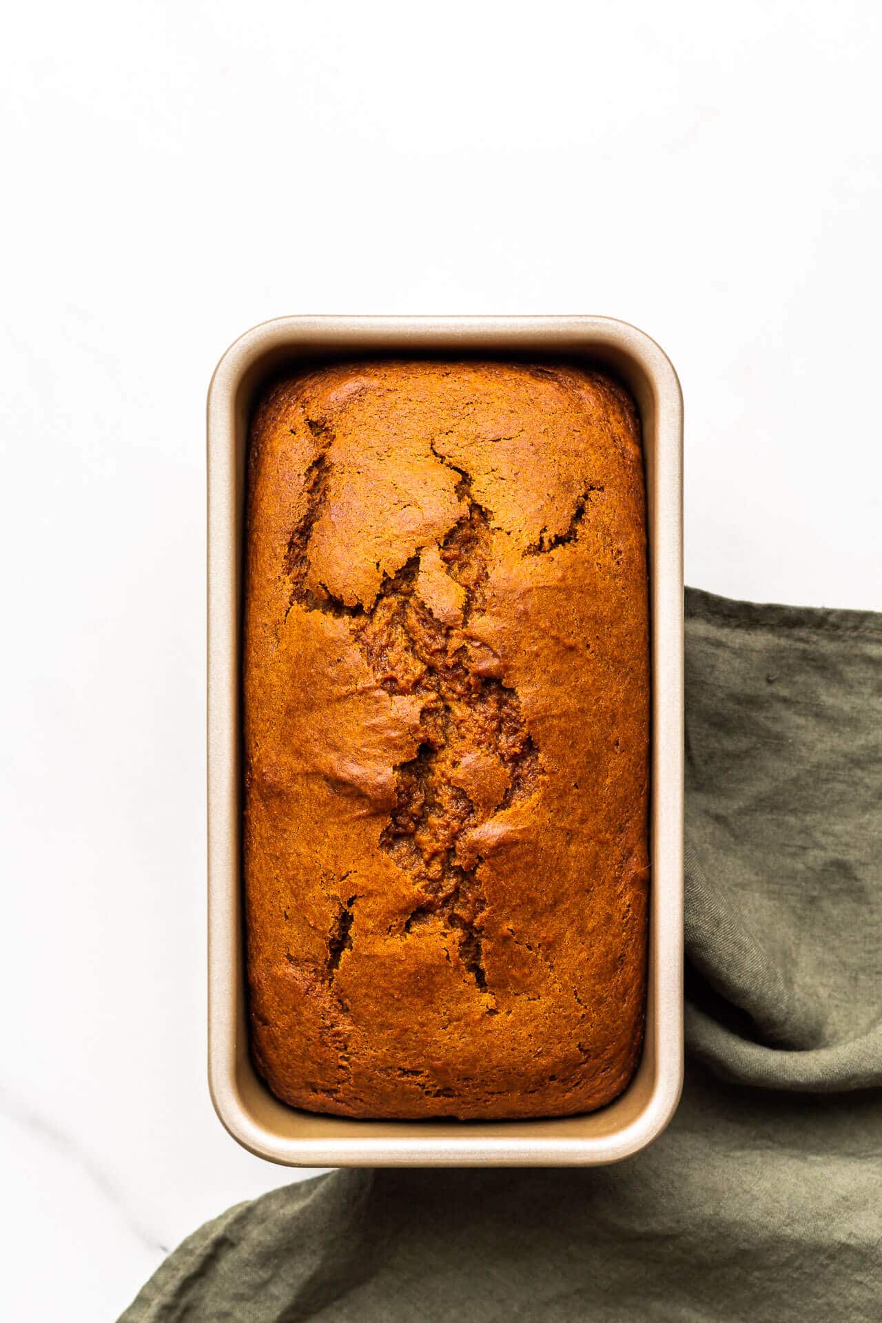 Pumpkin bread in loaf cake pan after baking with green linen.