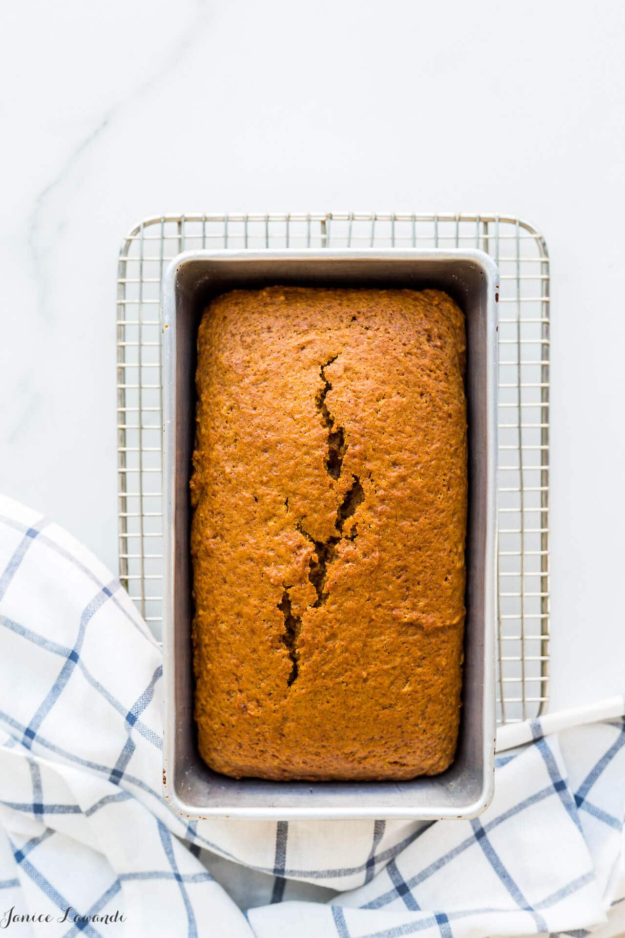 Pumpkin loaf cake in a 9x5 inch loaf pan set on a small cooling rack with a blue and white kitchen towel