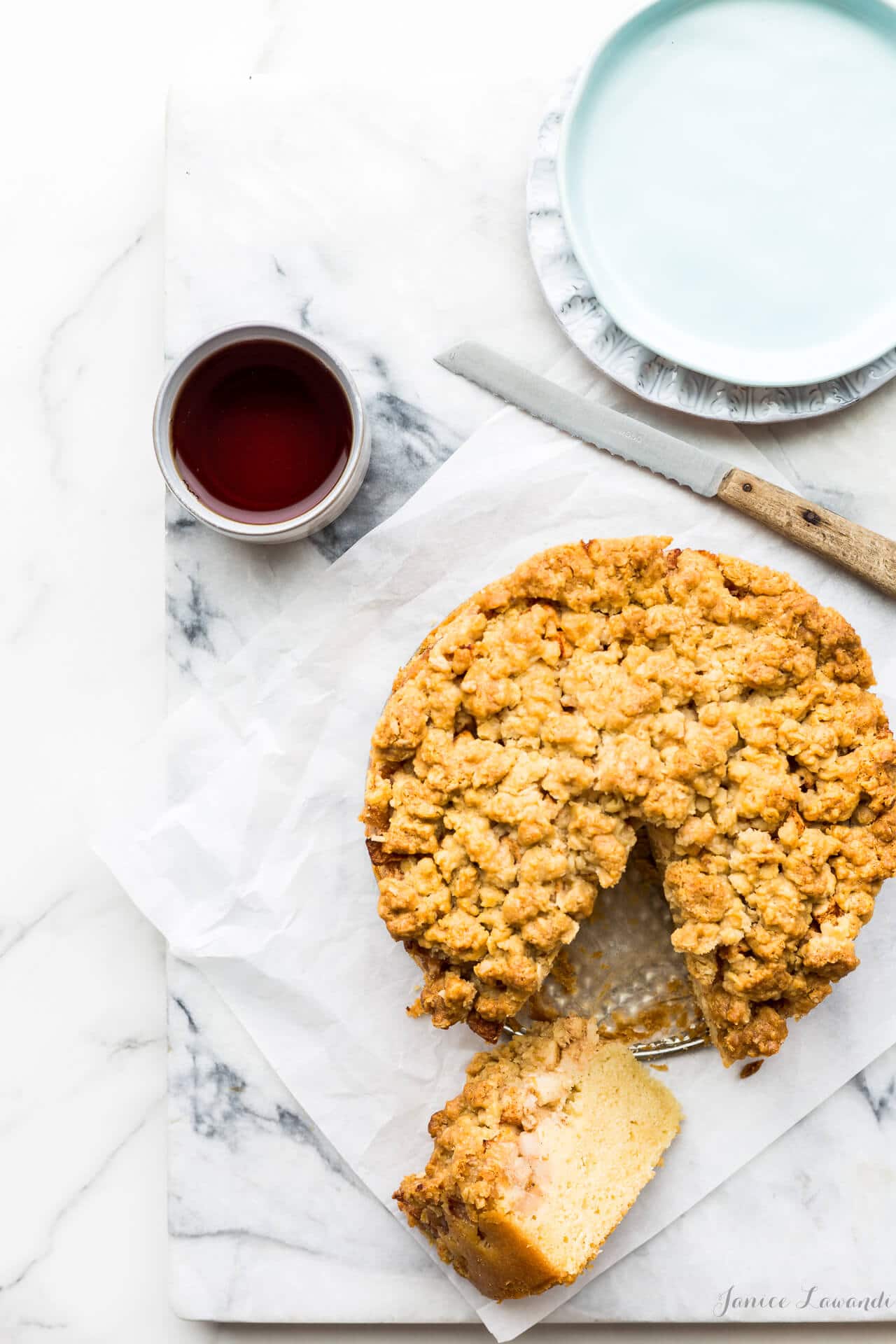 Apple crumb coffee cake ready to be served with cups of tea, plates and a serrated knife