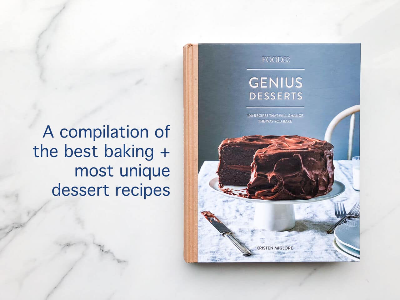 The cover of the Food52 Genius Desserts cookbook features a two layer chocolate cake with chocolate frosting on a cake stand