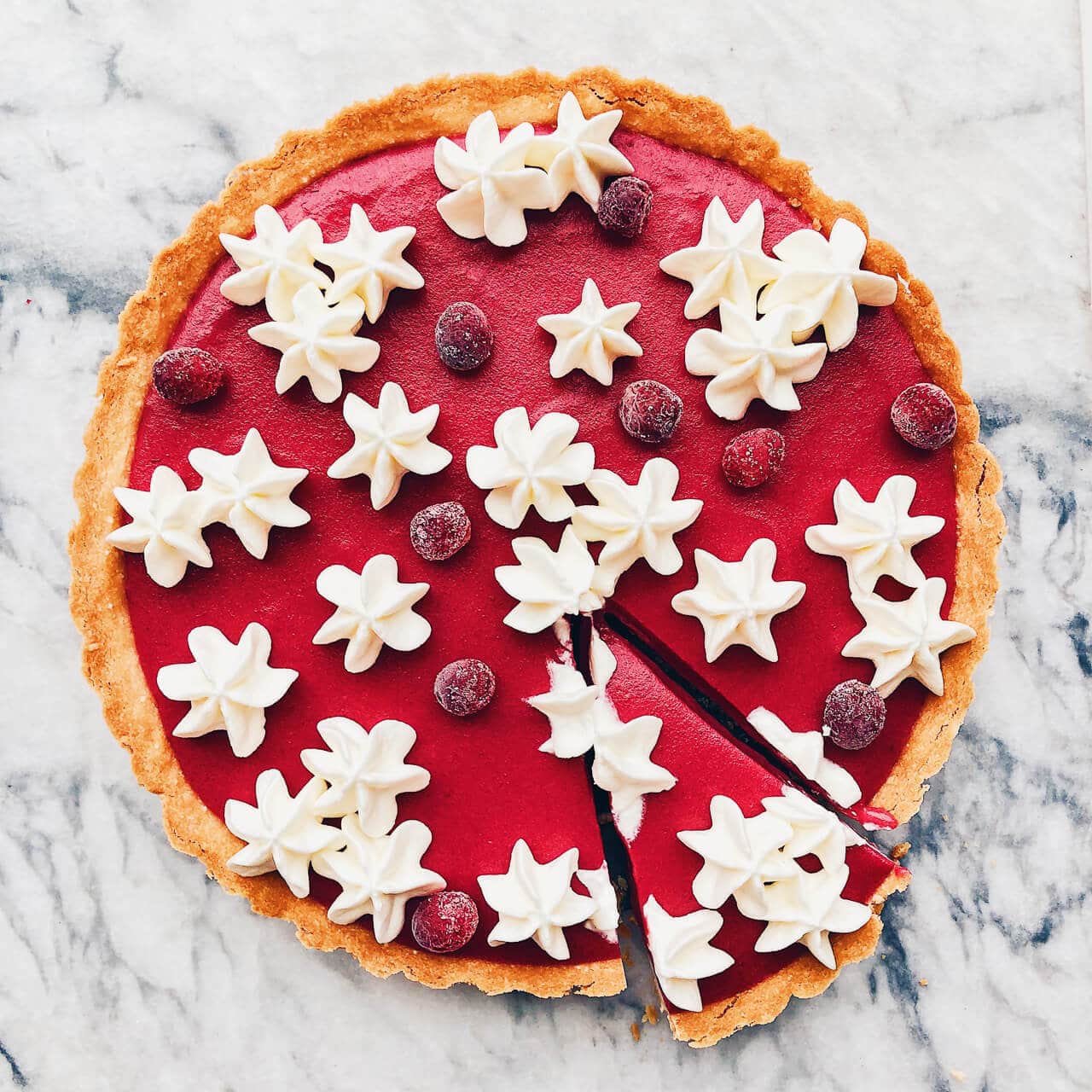 Cranberry curd tart with press-in shortbread crust baked in a fluted tart pan. Whipped cream is piped on the surface of the finished tart before serving