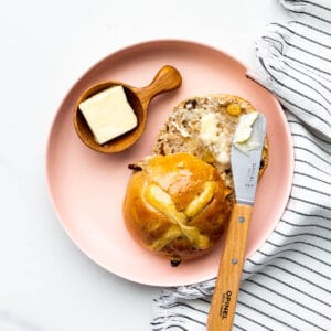 Hot cross bun on a pink plate split open and served with butter.